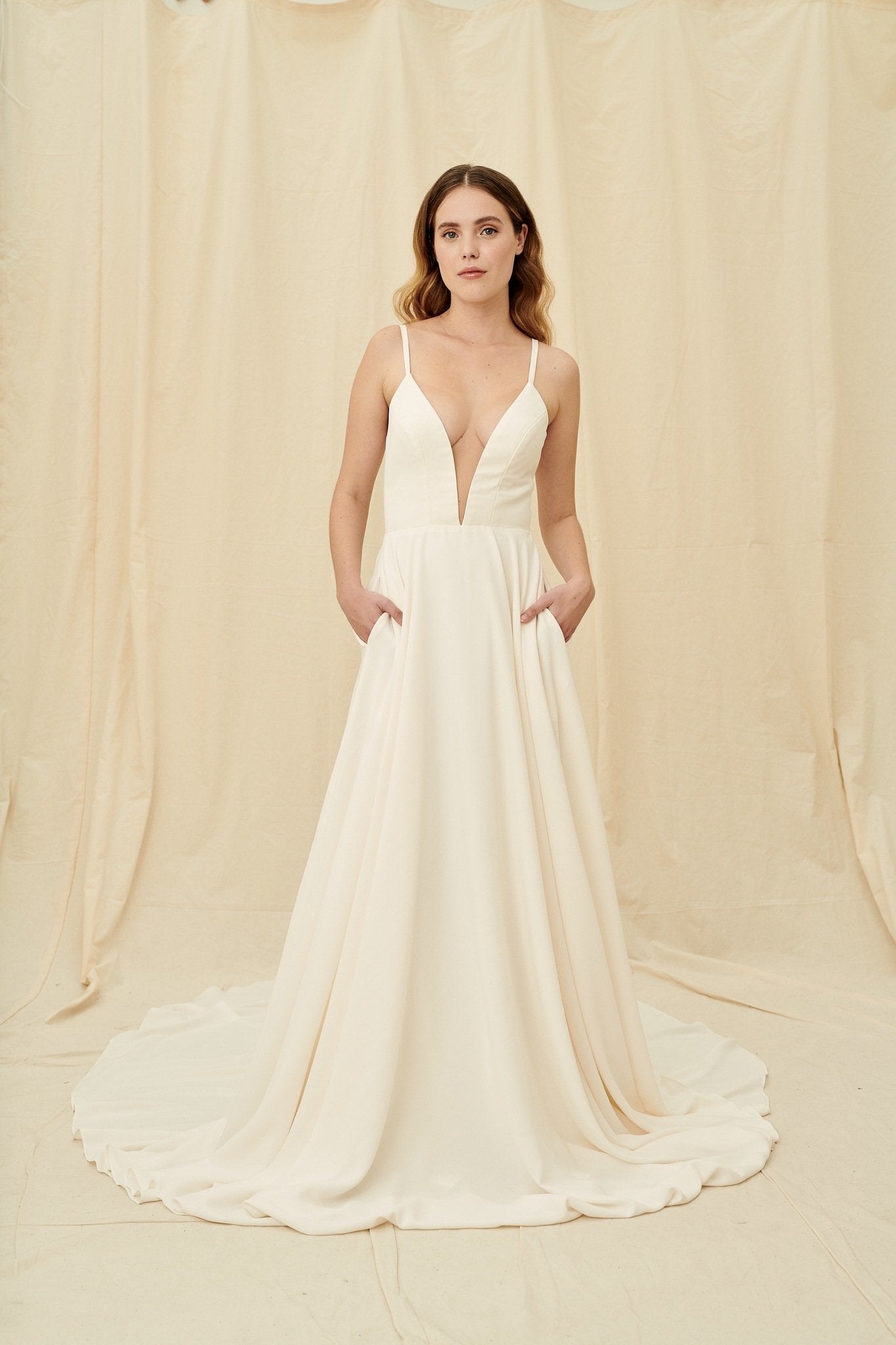 Super low cut crepe wedding dress with spaghetti straps, pockets, and a huge train